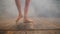 Young ballerina in costume with nude legs in pointe shoes on wooden stage floor to camera. Woman performs on dark