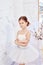 Young ballerina girl is preparing for a ballet performance. Little prima ballet. Girl in a white ball gown and Pointe near the wi