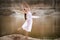 Young ballerina stands in a graceful pose on the edge of a sandy cliff against the background of the lake