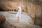 Young ballerina stands in a graceful pose on the edge of a sandy cliff against the background of the lake