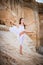 Young ballerina stands in a graceful pose on the edge of a sandy cliff against the background of the lake