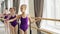 Young ballerinas in trendy ballet suits are practising arm movements and plie in light dancing hall with wooden ballet