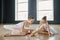 Young ballet teacher in white tutu helping youthful girl with pointe shoes