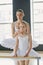 Young ballet teacher and youthful girl in white tutu standing in front of mirror