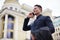 A young banker in a business suit talking on a mobile phone in the street against a bank background