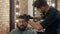 Young barber cutting hair to bearded male client in barbershop