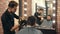 Young barber with hair clipper trimming male client in barbershop