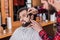 young barber in plaid shirt shaving man