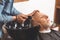 Young barber washing head of the aged client in the barbershop