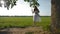 Young barefoot girl in a beautiful white rustic dress is swinging on a swing in the open field.