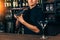 Young barman in bar interior shaking and mixing alcohol cocktail. Professional bartender portrait at work in night club
