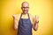 Young bartender man wearing barista apron working as professional over yellow background celebrating surprised and amazed for