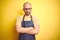 Young bartender man wearing barista apron working as professional over yellow background skeptic and nervous, disapproving