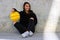 Young basketball player girl dressed in a black sweatshirt smiling and sitting in an urban court picking up a yellow basketball