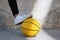 Young basketball player treading with her white shoe a yellow basketball in an urban court