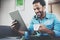 Young bearded African man using tablet while sitting on sofa and holding white cup coffee in hand at home.Concept people