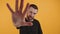 young bearded attractive European man extanding an opened hand towards the camera medium closeup orange background