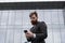 Young bearded Businessman holding mobile smartphone using app texting sms message wearing jacket outdoor. Successful