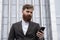 Young bearded Businessman holding mobile smartphone using app texting sms message wearing jacket outdoor. Successful