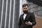 Young bearded Businessman holding mobile smartphone using app texting sms message wearing jacket outdoor. Successful