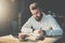 Young bearded businessman sits in cafe at table and writes in notebook.On table tablet computer, smartphone.Man is