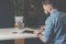 Young bearded businessman sits in office at table,using digital tablet and explores charts,making notes.