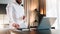 Young bearded businessman in white shirt is standing near desk in front of laptop, holding documents. Freelancer working