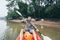 Young bearded Caucasian man paddling in kayak on Mekong river with water buffalo on background, Laos