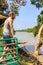 Young bearded guy in jeans shorts stands on the veranda of a bamboo hut on the riverbank