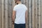 Young bearded hipster man dressed in white t-shirt and sunglasses is stands outdoor against wood wall. Mock up.