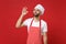 Young bearded male chef cook or baker man in striped apron white t-shirt toque chefs hat posing isolated on red