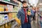 Young bearded man choosing bottled fresh juices in grocery section at supermarket