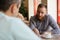 Young bearded man explain and discuss something with his interlocutor friend sitting indoors cafe with cup of coffee