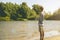 Young bearded man fishing standing on the sandy river bank with fish-rod during summer d