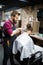 Young bearded man getting haircut by hairdresser with electric razor at barber shop