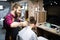 Young bearded man getting haircut by hairdresser with electric razor at barber shop