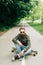 Young bearded man longboarder in casual clothes sitting on the longboard or skateboard outdoors, side view. Urban, subculture,