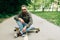 Young bearded man longboarder in casual clothes sitting on the longboard or skateboard outdoors, side view. Urban, subculture,