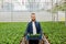 A young bearded man stands in a greenhouse, holding boxes of plants in his hands