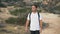 Young bearded man travelling with backpack in hills. Lonely tourist puts his hand to eyes looking far. Active leisure of