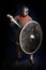 Young bearded man in a Viking-era helmet standind and holding a sword and shield