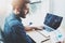 Young bearded man working at sunny loft office on laptop.Businessman analyze paper documents reports in his hand.Blurred