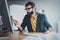 Young bearded man working at sunny office on desktop computer while sitting at wooden table.Businessman analyze stock