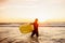 Young bearded surfer in wetsuit with yellow surfing longboard walk from water at sunset ocean. Water sport adventure camp and