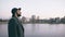 Young bearded tourist man in hat and coat watching cityscape and daydreaming while standing on riverside