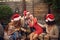 Young beardy guy hugging attractive blonde at Christmas party, wearing santa hat with other friends gathered