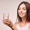 Young beatiful girl hold water glass. Hydrate female face. Happy women indoors