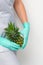 Young beautician wearing blue gloves in uniform with pineapple covers an intimate area on a white background, bikini