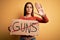 Young beautiful activist woman asking for peace holding banner with stop guns message with open hand doing stop sign with serious