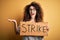 Young beautiful activist woman with curly hair and piercing protesting in strike holding poster very happy and excited, winner